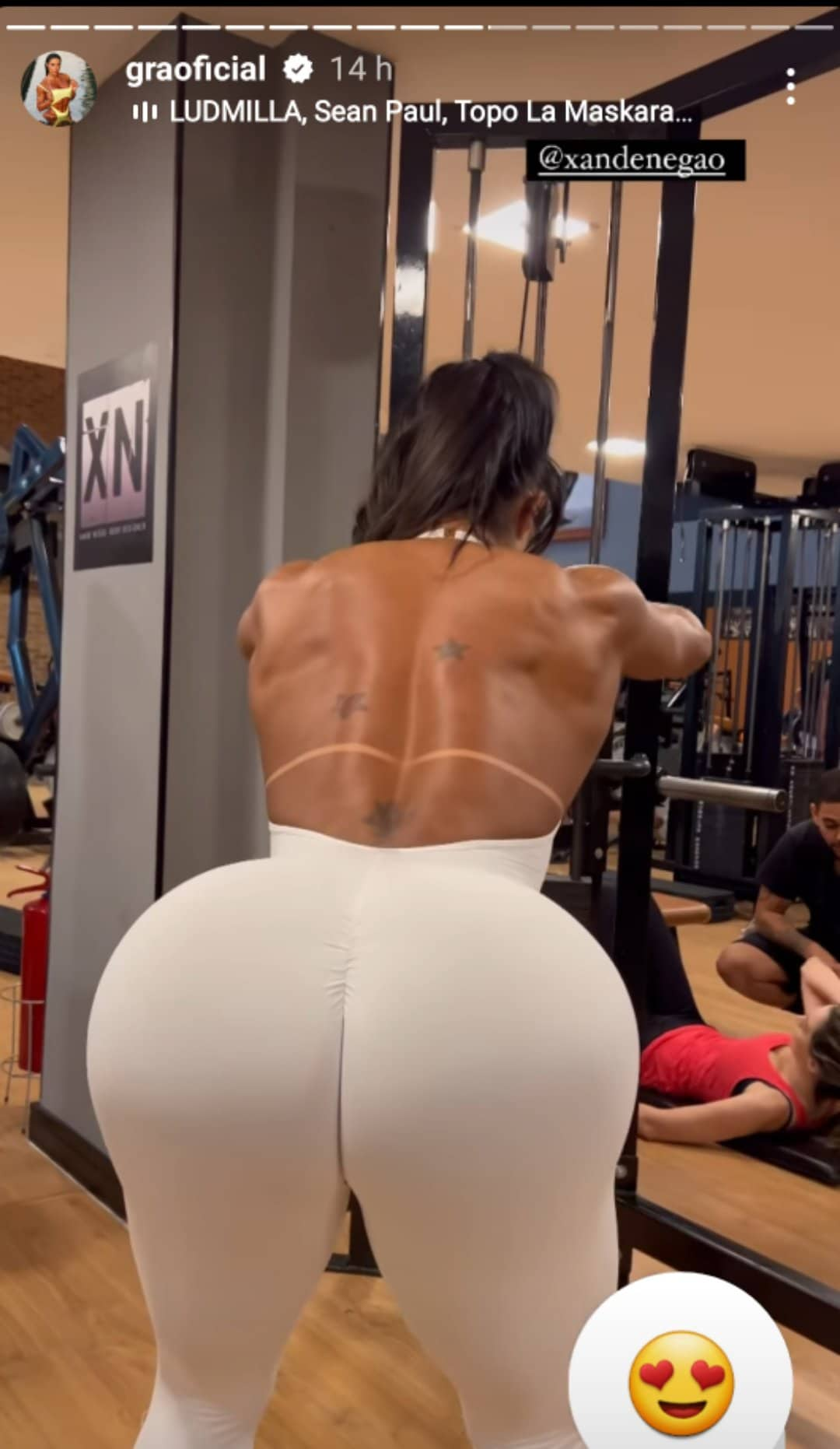 Gracyanne Barbosa treinando na academia em um registro feito de costas, com foco no seu bumbum. A influenciadora usa um macacão branco coladíssimo no corpo e aberto nas costas