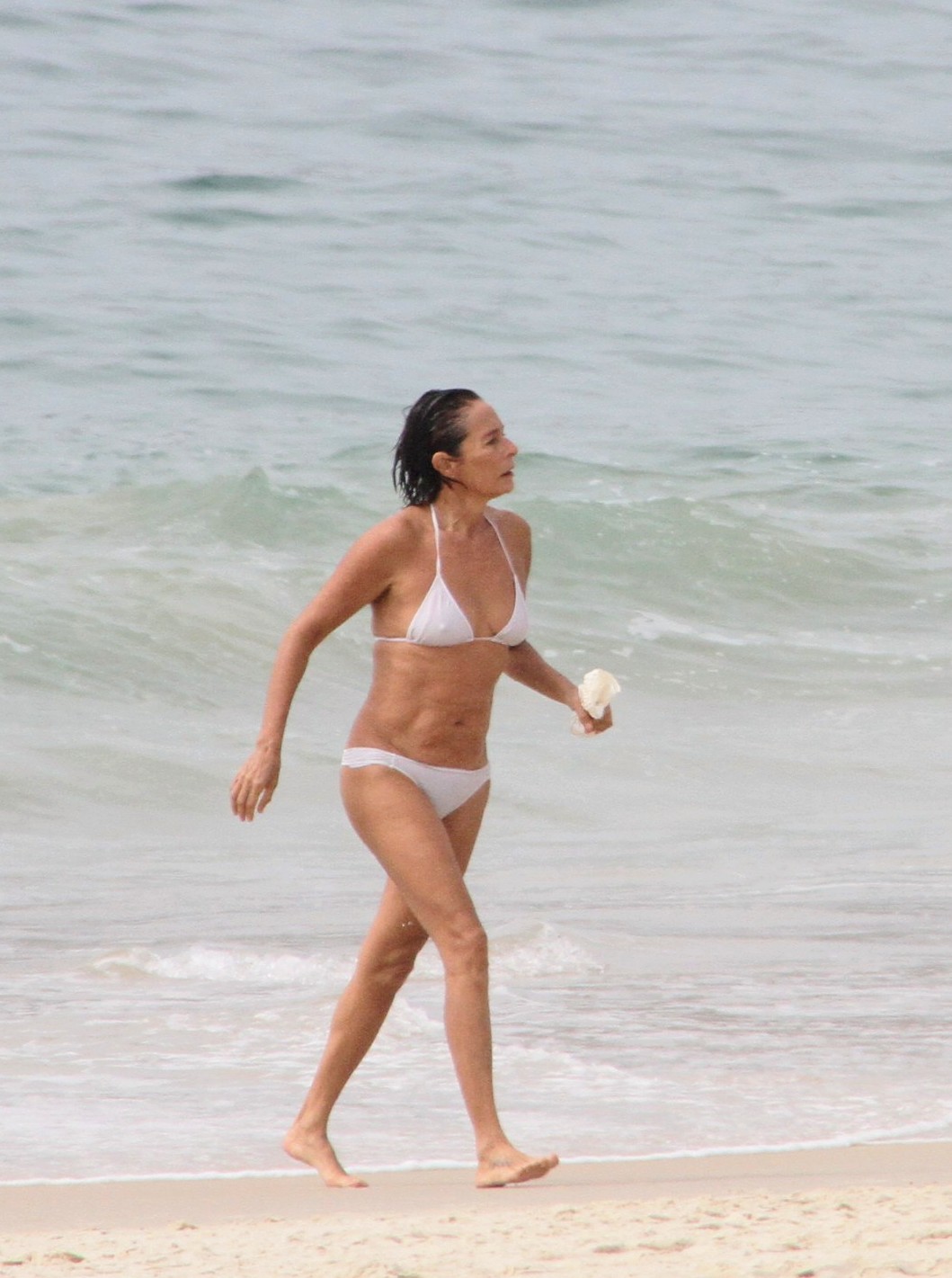 Foto de Andréa Beltrão andando na praia de biquíni branco