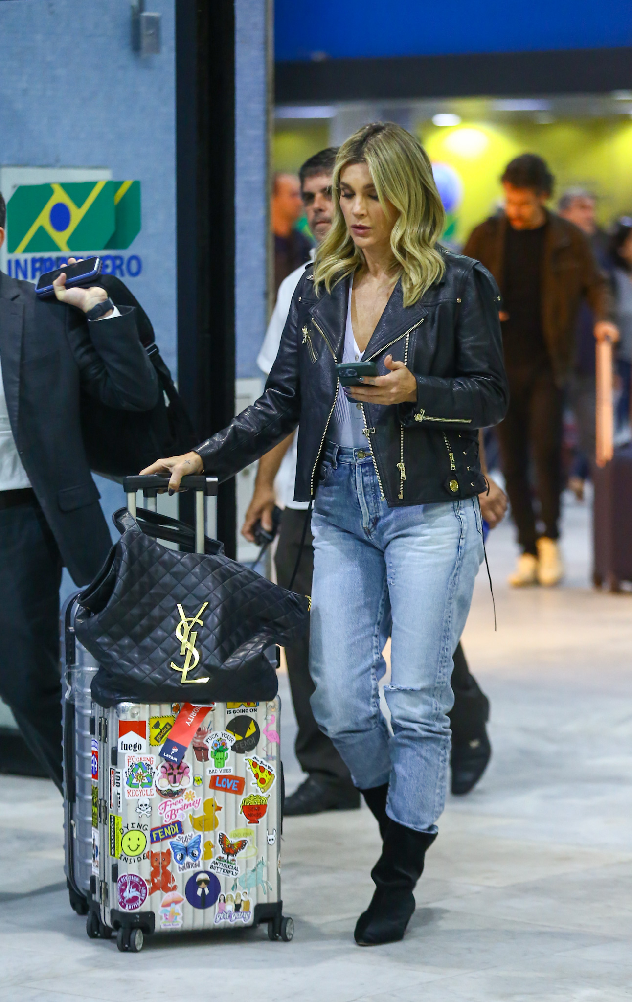 Foto de Flávia Alessandra desembarcando em aeroporto do Rio de Janeiro com jaqueta de couro e regata decotada