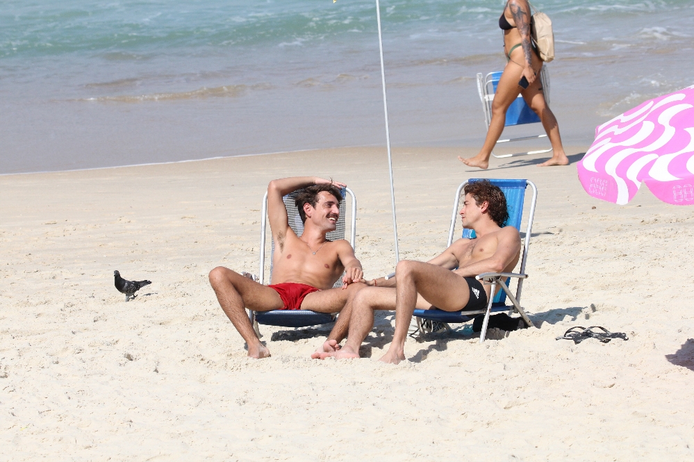 Foto do ator Jesuíta Barbosa sentado junto de um rapaz na praia