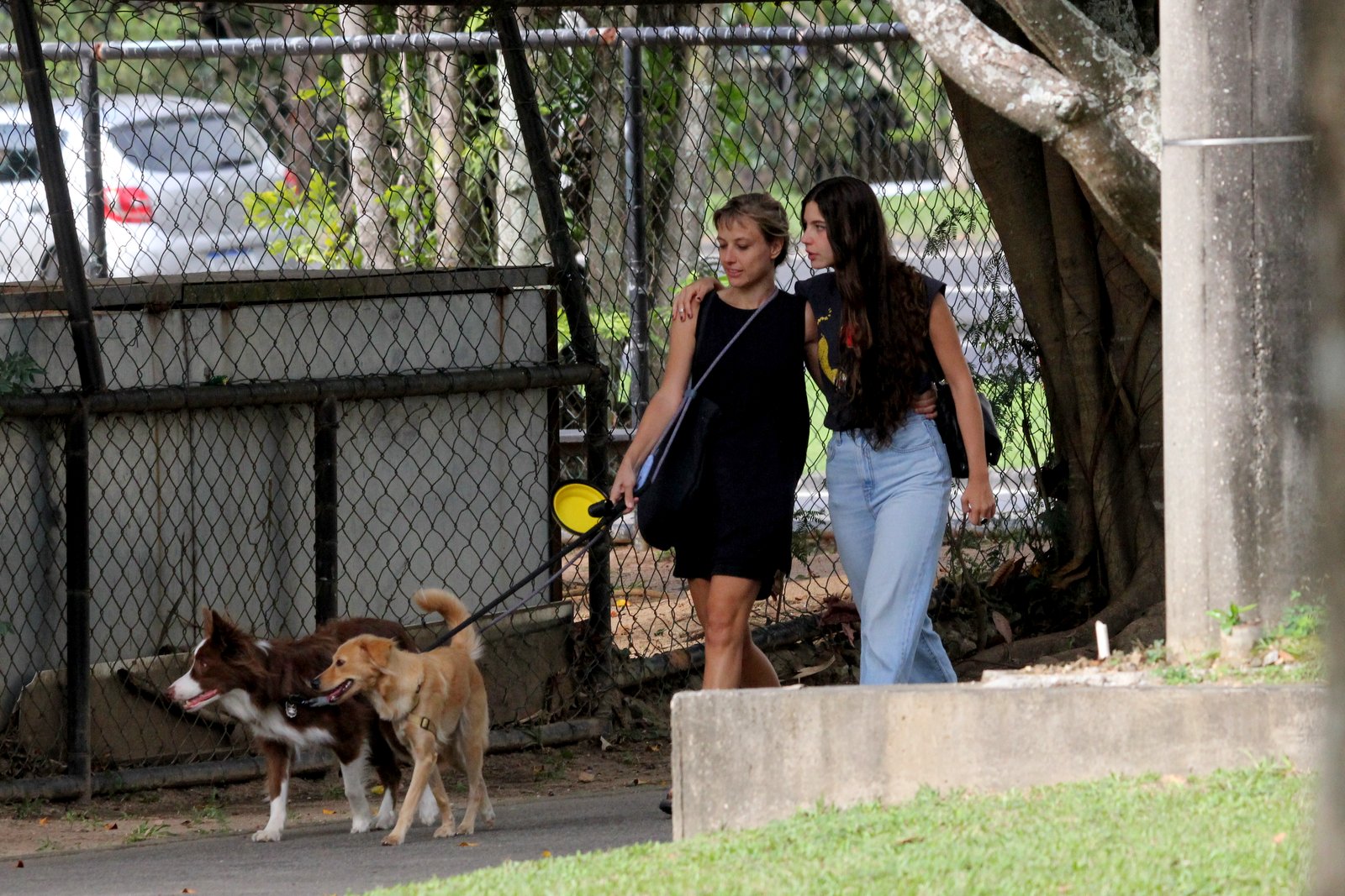 Foto de Alanis Guillen abraçada a uma mulher loira enquanto anda por um parque levando cachorros para passear