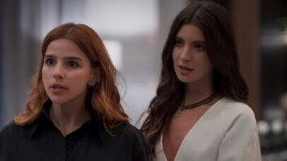 Duas mulheres jovens, uma com cabelo ruivo e outra com cabelo castanho escuro, em um ambiente interno. A mulher ruiva usa um…