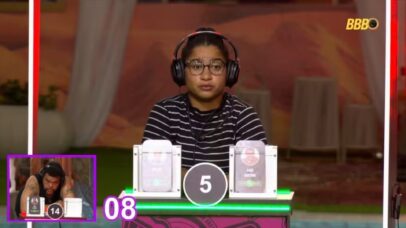 Participante do BBB 23 com fones de ouvido e óculos, em frente a um jogo. Ao fundo, outro participante em um telão.